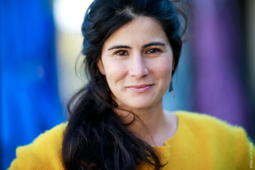 Carole Pia avec les cheveux détachés sourit devant l'objectif de l'appareil photo, derrière elle un fon flou