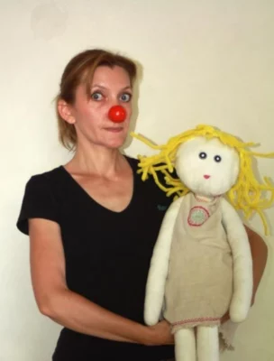 La comédienne et chanteuse Magali Braconnot pose en intérieur devant un mur blanc et une poupée à la main