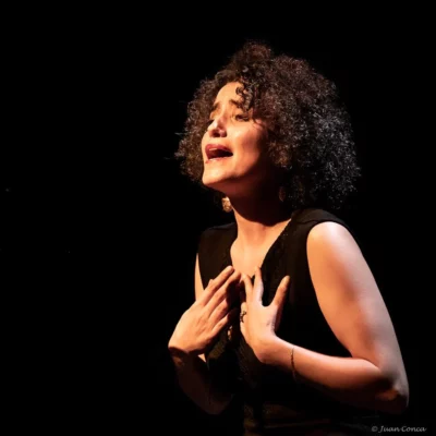 Une femme sur un fond noir illuminée par une lumière dorée en train de chanter
