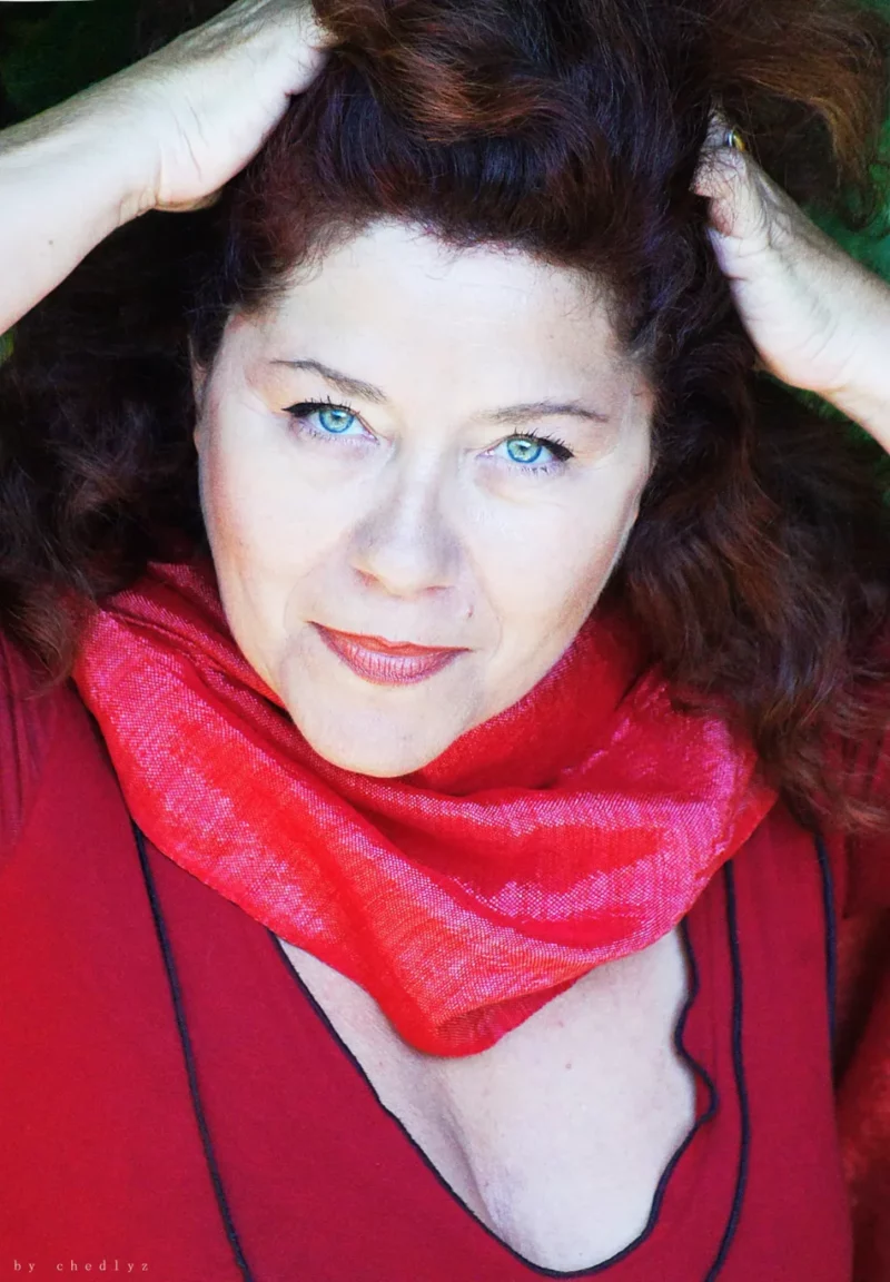 La comédienne Catherine Lecoq habillée en rouge regarde droit devant avec les mains sur les cheveux
