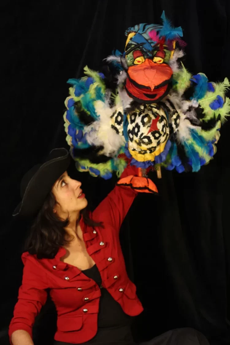 Photo de scène où la marionnettiste et comédienne Chiara Caruso manipule une de ses créations, un oiseau multicolore
