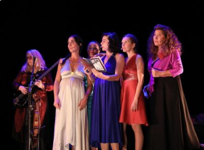 Un groupe de femme bien habillées sur une scène noir devant un micro