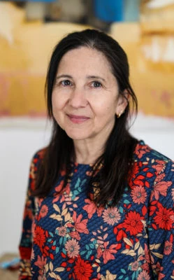 Une femme souriante avec une chemise à fleurs regarde droit dans la caméra