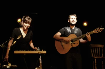 Un homme qui joue la guitare et une femme qui joue le piano électrique lors d'un concert 