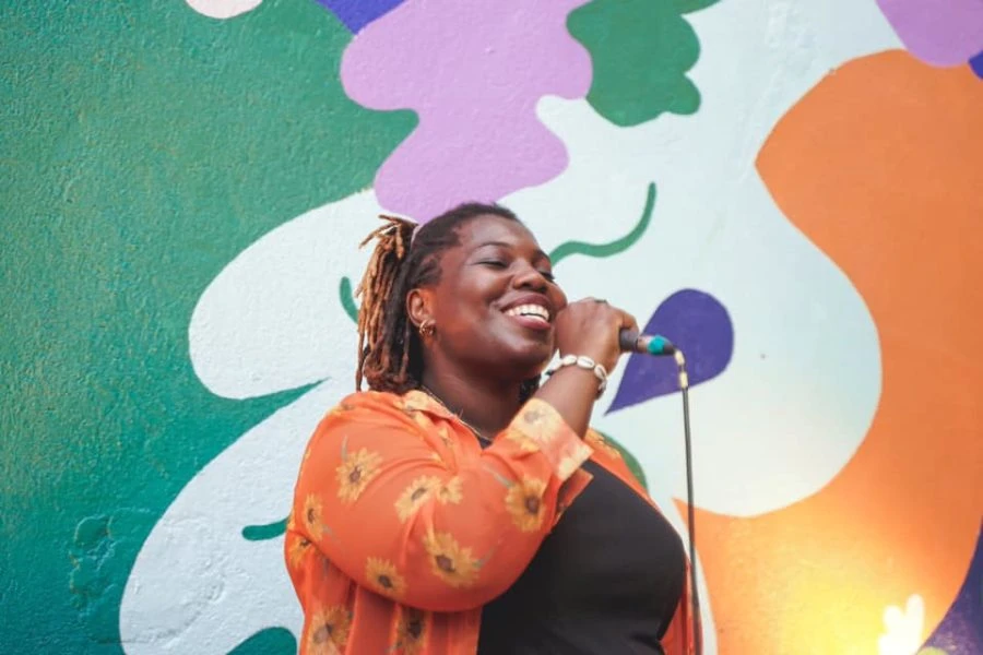 La rappeuse et autrice Erika Nomeni souriante et avec un microphone à la main, derrière elle un mur décoré