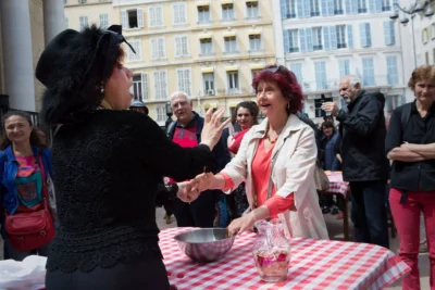 En externe, une femme habillé en noir de dos reçoit des personnes derrière à une table avec une nappe à carreaux rouges et blancs