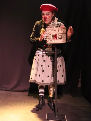 Véronique Martin en clowne sur scène derrière une cage à oiseaux