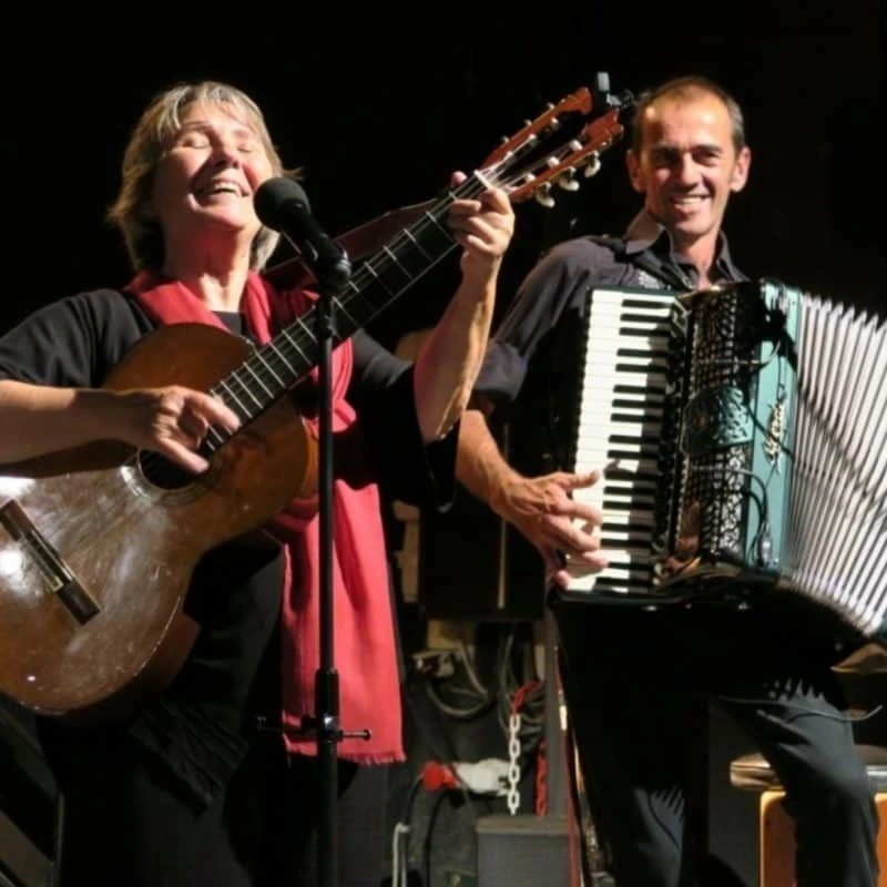 Sur un scène musicale, une femme joue la guitare, accompagné par un homme à l'accordéon