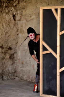 La metteure en scène, comédienne et clown Véronique Martin déguisée en clowne surgit de derrière un écran