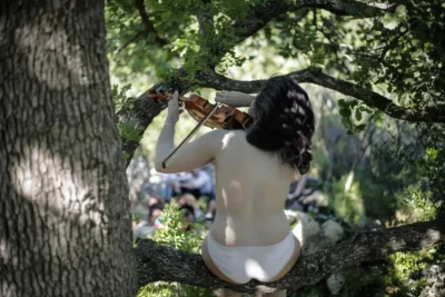 Une femme assise de dos sur une branche en train de jouer un violon