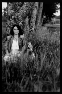 Une femme assise en pleine nature, adossée à un arbre avec une guitare à côté d'elle