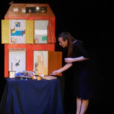 Stéphanie Joire, chanteuse et comédienne, en train de jouer, à côté d'une grande maison en papier