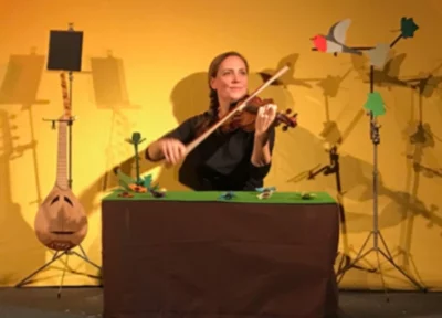 Stéphanie Joire, chanteuse et musicienne, en train de jouer le violon sur scène, assise derrière une table