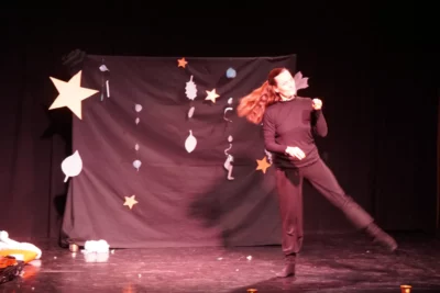 Sur une scène noir, une femme habillée en noir est en train de danser