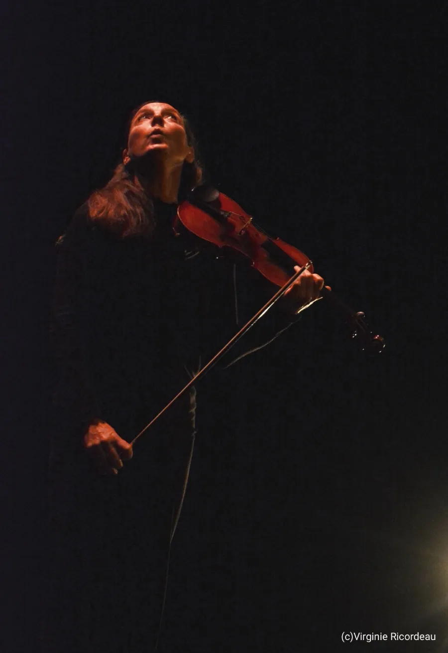 Une femme dans le noir, avec un violona à la main, regarde en haut