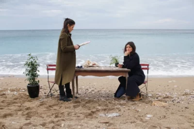 Deux femmes autour d'une table au bord de mer. L'une est assise, l'autre debout,derrière elle une plante d'intérieur