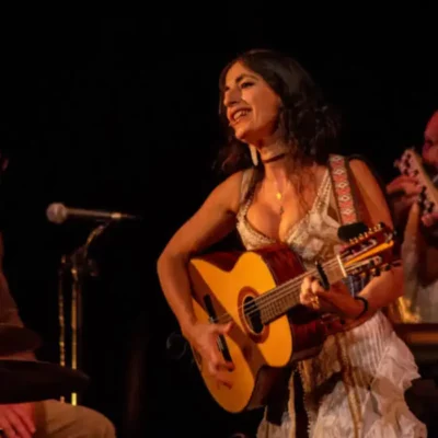 Sur une scène musicale, une femme joue la guitare et chante devant un micro