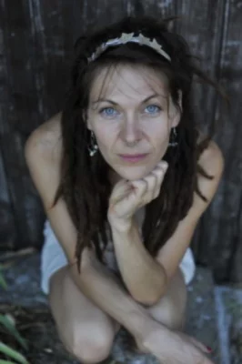 Julie Ettabaâ, artiste musicale, pose pour un portrait en extérieur, accroupie au sol avec le regarde direct dans l'objectif