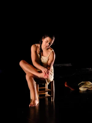 Une femme assise sur une scène de théâtre : une des interprètes du spectacle de théâtre-danse Farmor Mamita
