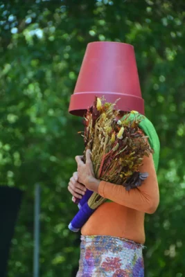 Une personne de profil avec un seau sur la tête et un bouquet de fleurs en main