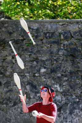 Une femme aux lunettes de soleil et chapeau large en train de jongler avec des massues