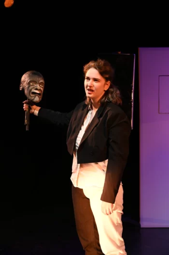 La comédienne Lunell Odelin Toussaint sur scène avec une marionnette représentant une t^te dans sa main droite