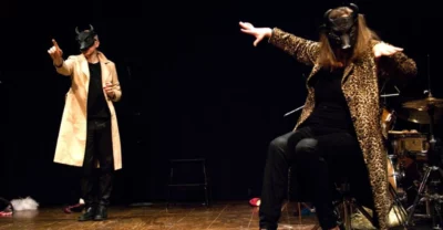 Deux personnages masqués dansent sur une scène de théâtre