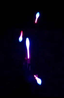 Quatre massues lumineuses qui voltigent dans l'air sur un fond noir