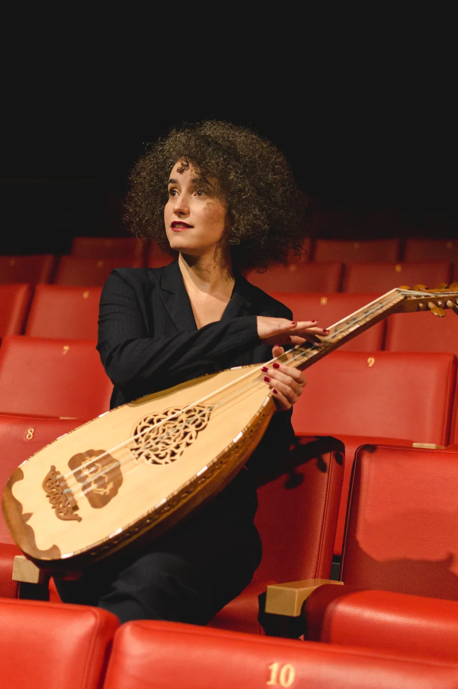 Une femme habillée en noir avec un instrument à cordes au milieu d'une rangée de fauteuils rouges