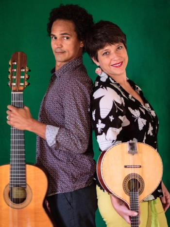 Un homme avec une guitare et une femme avec une mandoline posent dos contre dos sur un fond vert