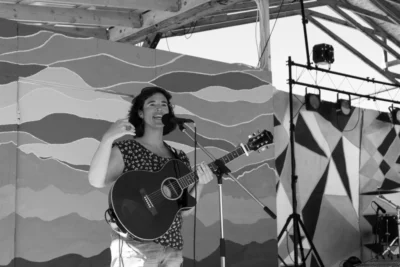 Iz Alors, musicienne, dans une photo en noir et blanc en train de chanter et jouer la guitare