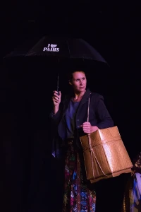 Sur un fond noir, une femme avec un parapluie et un sac en bambou regarde hors-champ