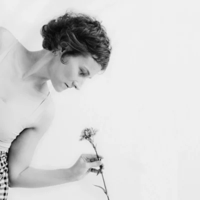 Une femme aux cheveux courts, de profil, se penche vers le bas avec une fleur entre les doigts