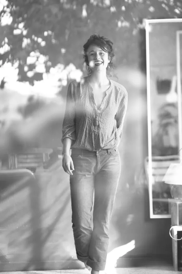 Photo en noir et blanc d'une jeune femme souriante derrière une vitre