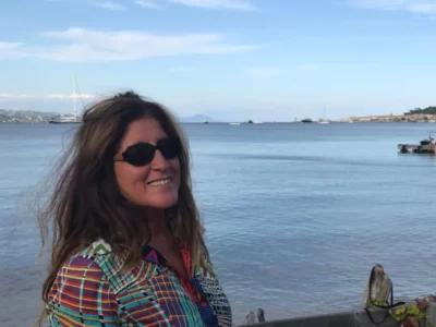 Une femme souriante avec des lunettes de soleil et la mer derrière elle