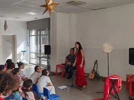 Une femme habille en rouge chante au micro devant un public d'enfants