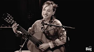 Une jeune femme souriante assise devant un micro avec une guitare sous le bras