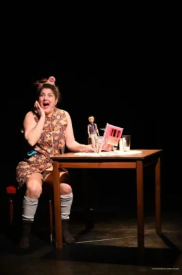 Une femme assise sur une chaise à côte d'une table avec une poupée à la main