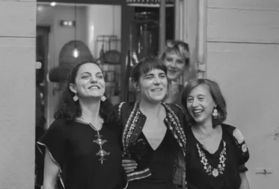 Photo en noir et blanc de trois jeunes femmes souriantes, habillées en tenue traditionnelle