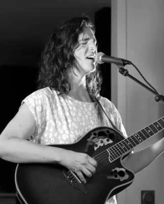 Photo en noir et blanc d'une femme en train de jouer la guitare et chanter devant un micro