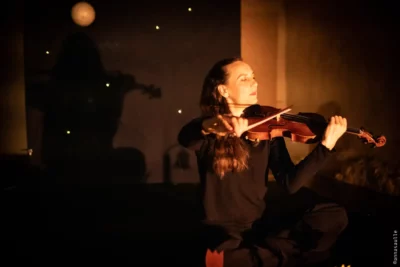 Une femme assise sur le plateau d'une scène de théâtre en train de jouer du violon