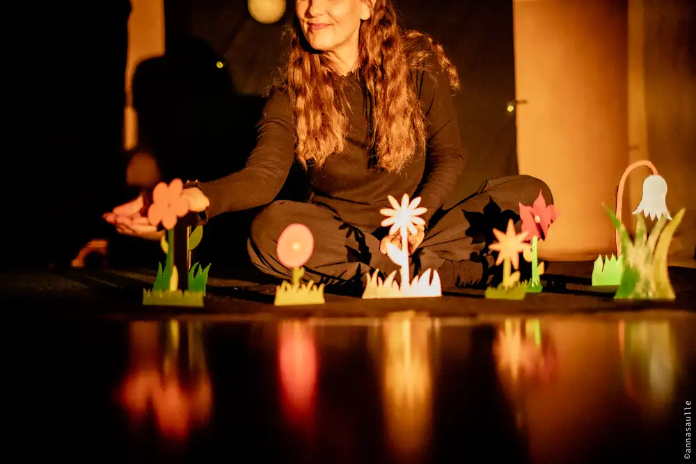 Une femme assise sur un scène de théâtre qui montre un jardin de fleurs en carton