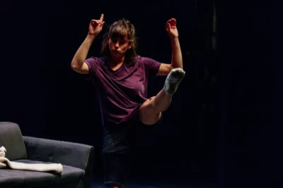 Une jeune femme sur une scène de théâtre tend une jambe en l'air devant elle tandis que ses bras se lèvent vers le haut