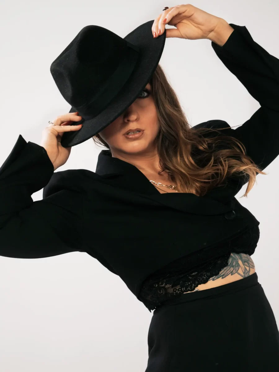 Une femme en pose plastique, habillée en noir avec un chapeau qui lui couvre le visage