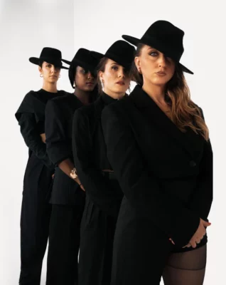 Quatre femmes habillées en noir, avec un chapeau, disposées en diagonal