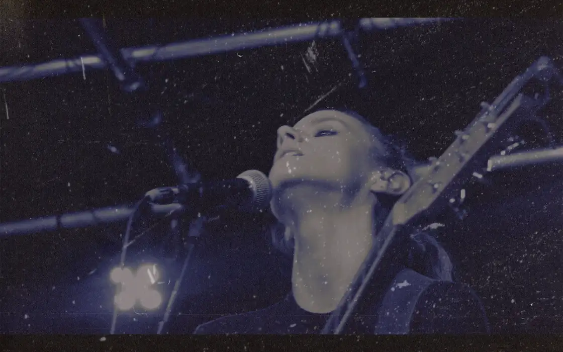 Photo en gros plan et en contre-plongée d'une jeune femme devant un micro, avec une guitare dans les bras