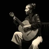 Photo en noir et blanc d'une jeune femme assise, en train de jouer la guitare