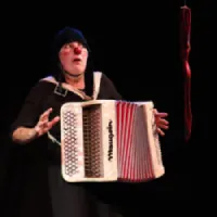 Un personnage clownesque en train de jouer un accordéon dans un fond noir