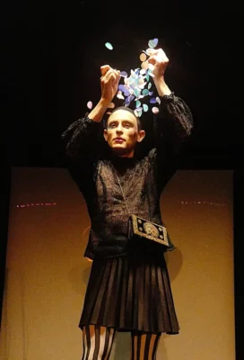 Sur un scène de théâtre, un homme aux bras levés fait tomber des morceaux de papier coloré