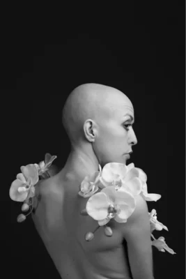 Une jeune femme au crâne rasé, de dos, avec des fleurs qui couvrent ses épaules nus